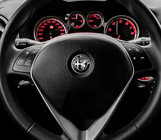 Close-up of the Alfa Romeo steering wheel and illuminated dashboard, serviced at Exotic Auto Services workshop.