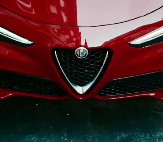 Close-up of the front grille and logo of a red Alfa Romeo serviced at Exotic Auto Services workshop.